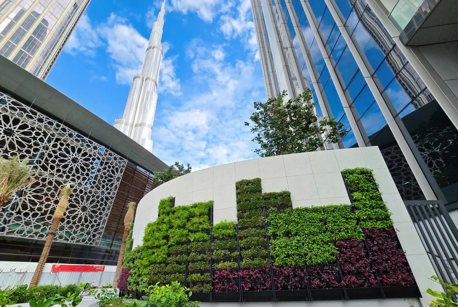 The Plot B4 living wall in stepped green and copper blocks, with the Burj Khalifa and a mashrabiya screen behind it