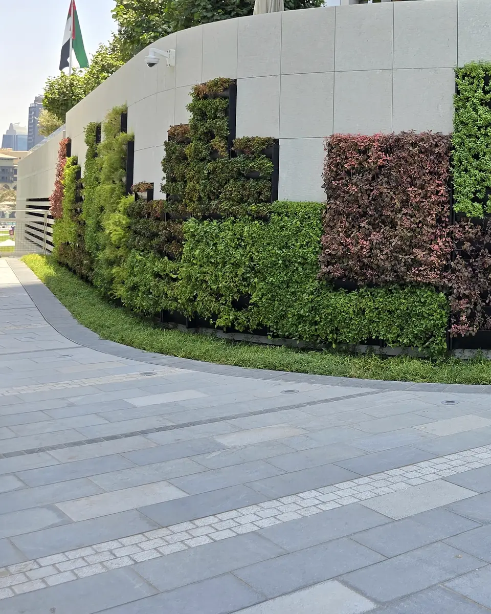 The wall curving away along the pedestrian approach, planted modules meeting pale stone cladding