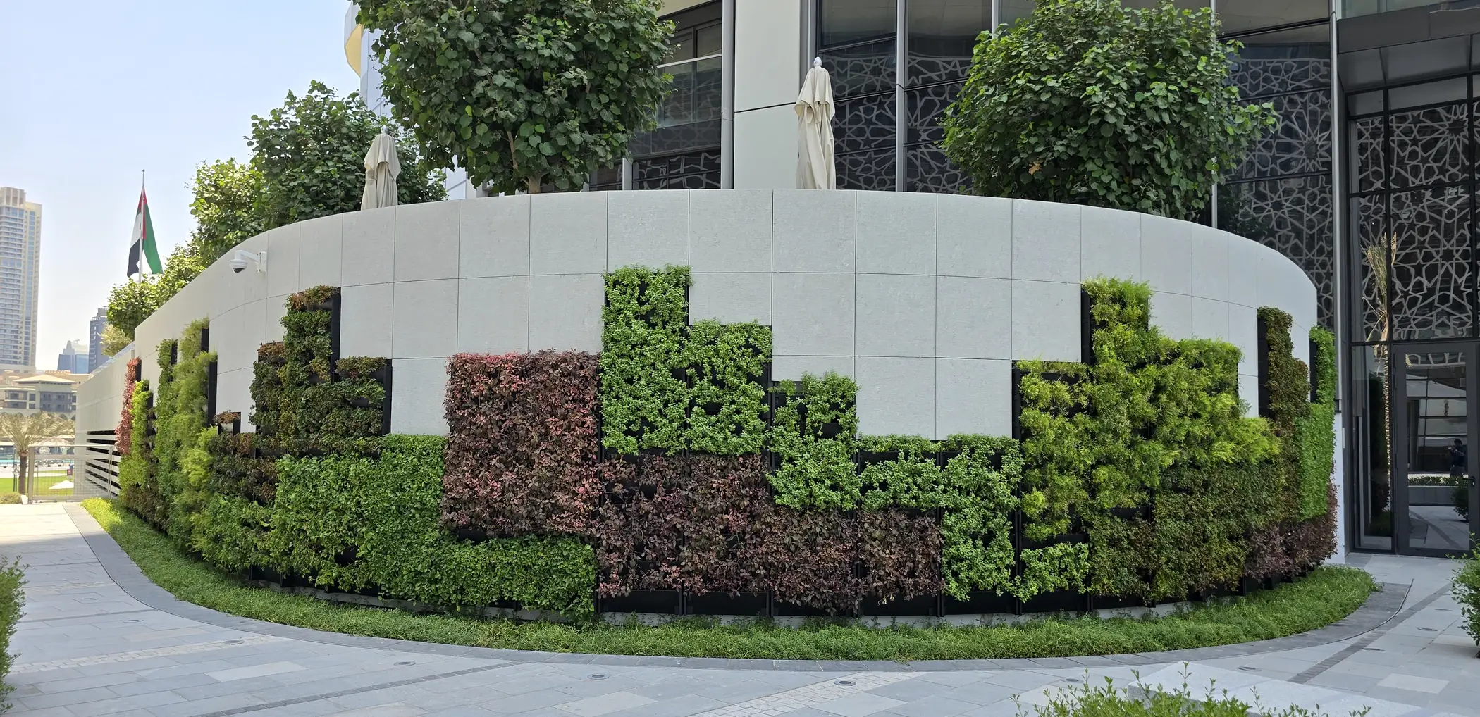 The curved PlantBox wall wrapping the podium of Plot B4, planted in stepped blocks of green and copper foliage